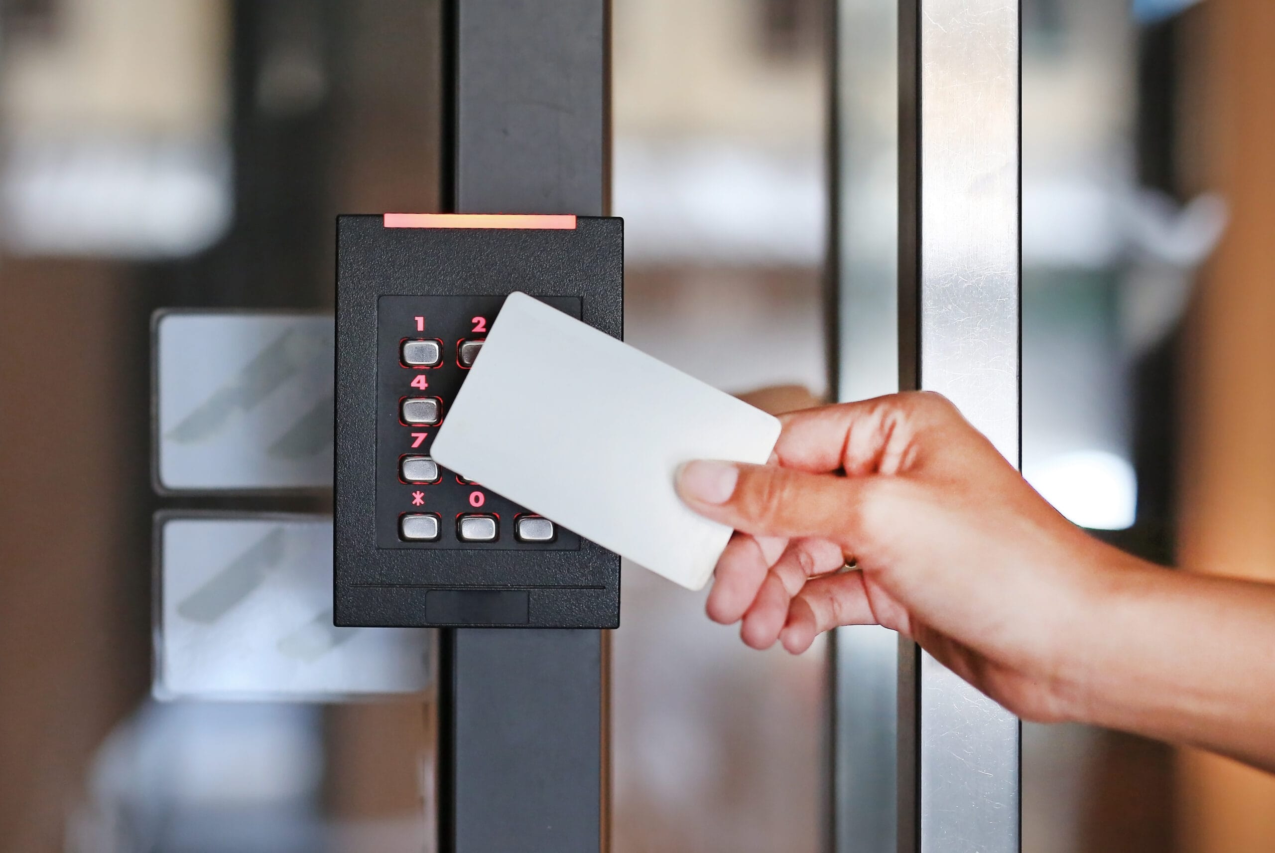 Hand holding an access card to a keypad reader on a glass door frame