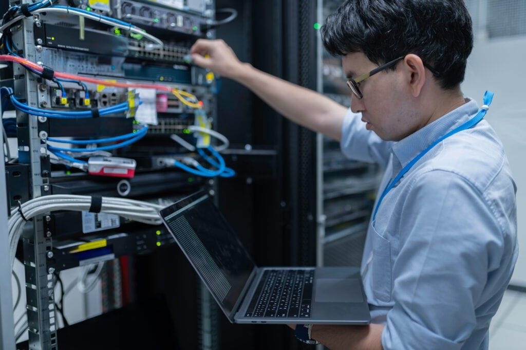 Technician holding a laptop while working on cabled rack equipment