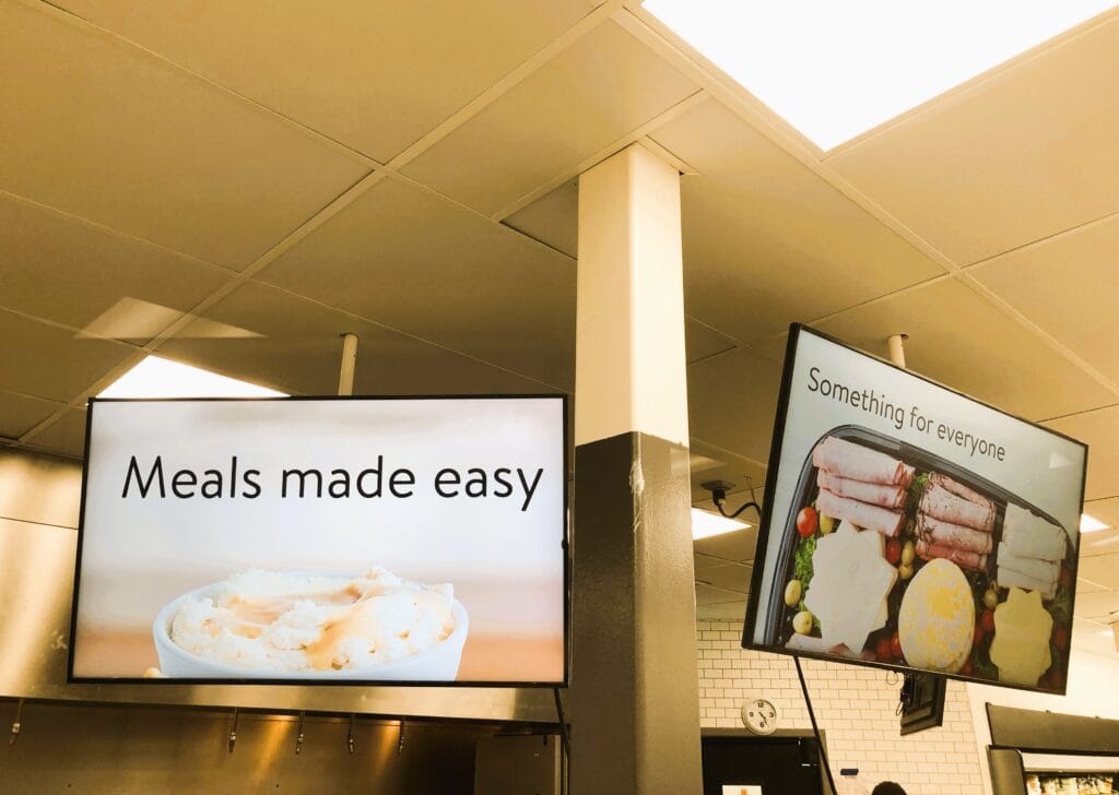Two ceiling-mounted display screens above a retail service area