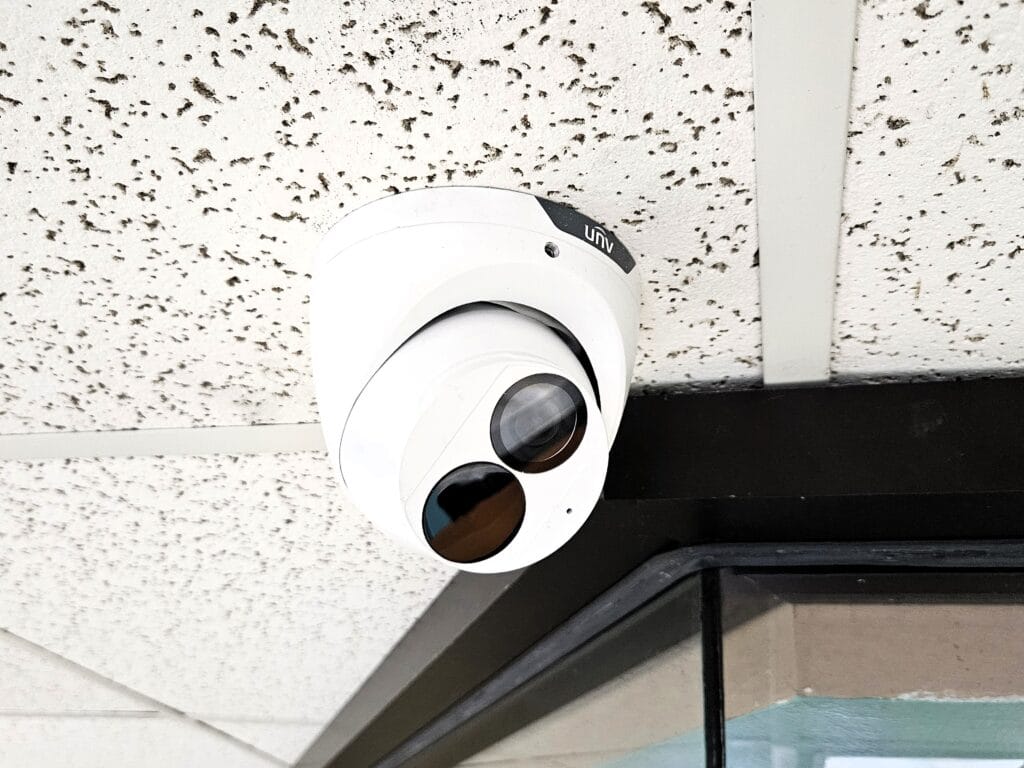 White dome camera mounted above a black-framed glass door