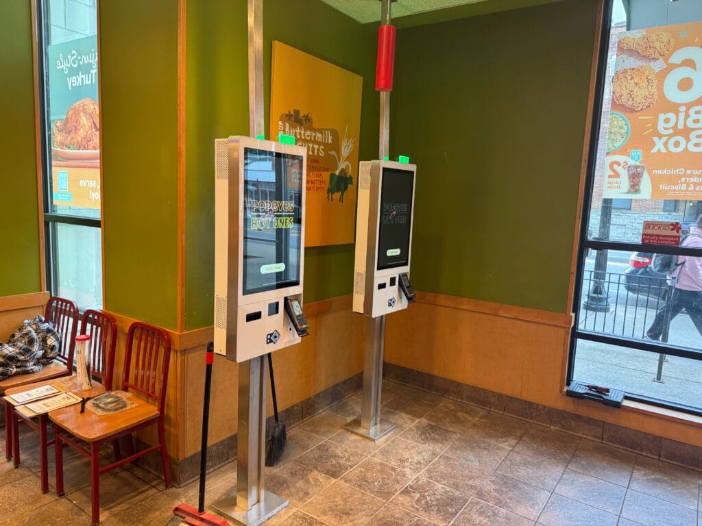 Two self-order kiosks on floor stands in a restaurant dining area