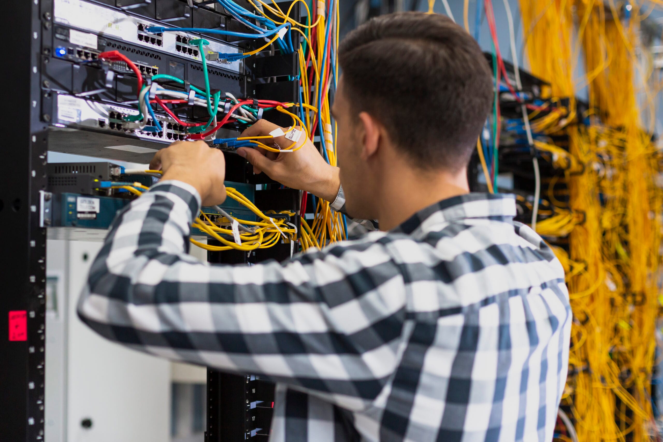 Technician connecting cables into rack switches surrounded by bundled Ethernet cabling